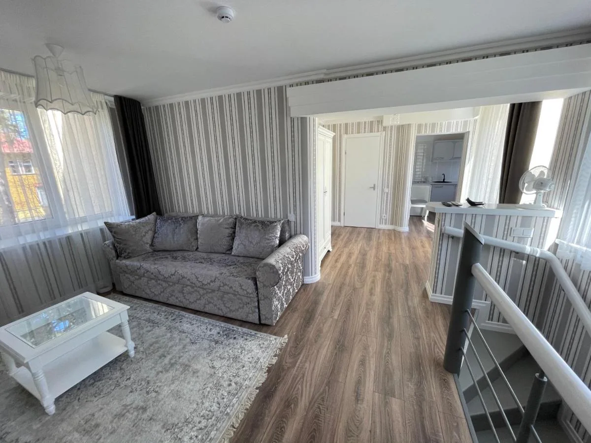 Svetainė su sofa ir kavos staliuku, gilumoje — virtuvė ir laiptų turėklai