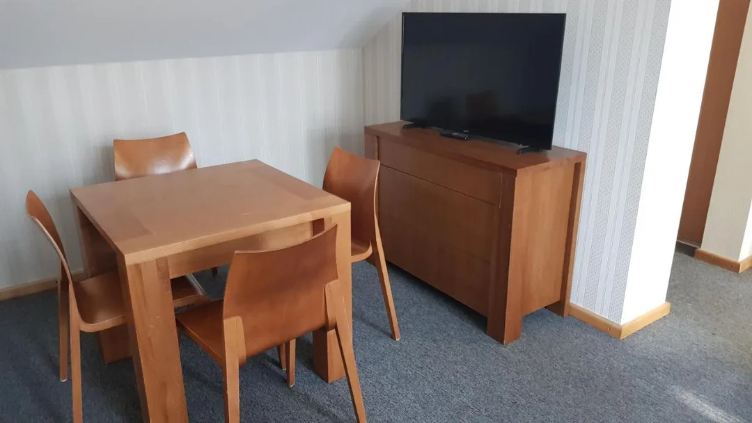 Stalas su keturiomis kėdėmis ir televizorius ant komodos