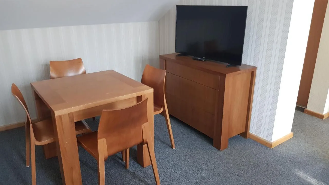 Stalas su keturiomis kėdėmis ir televizorius ant komodos