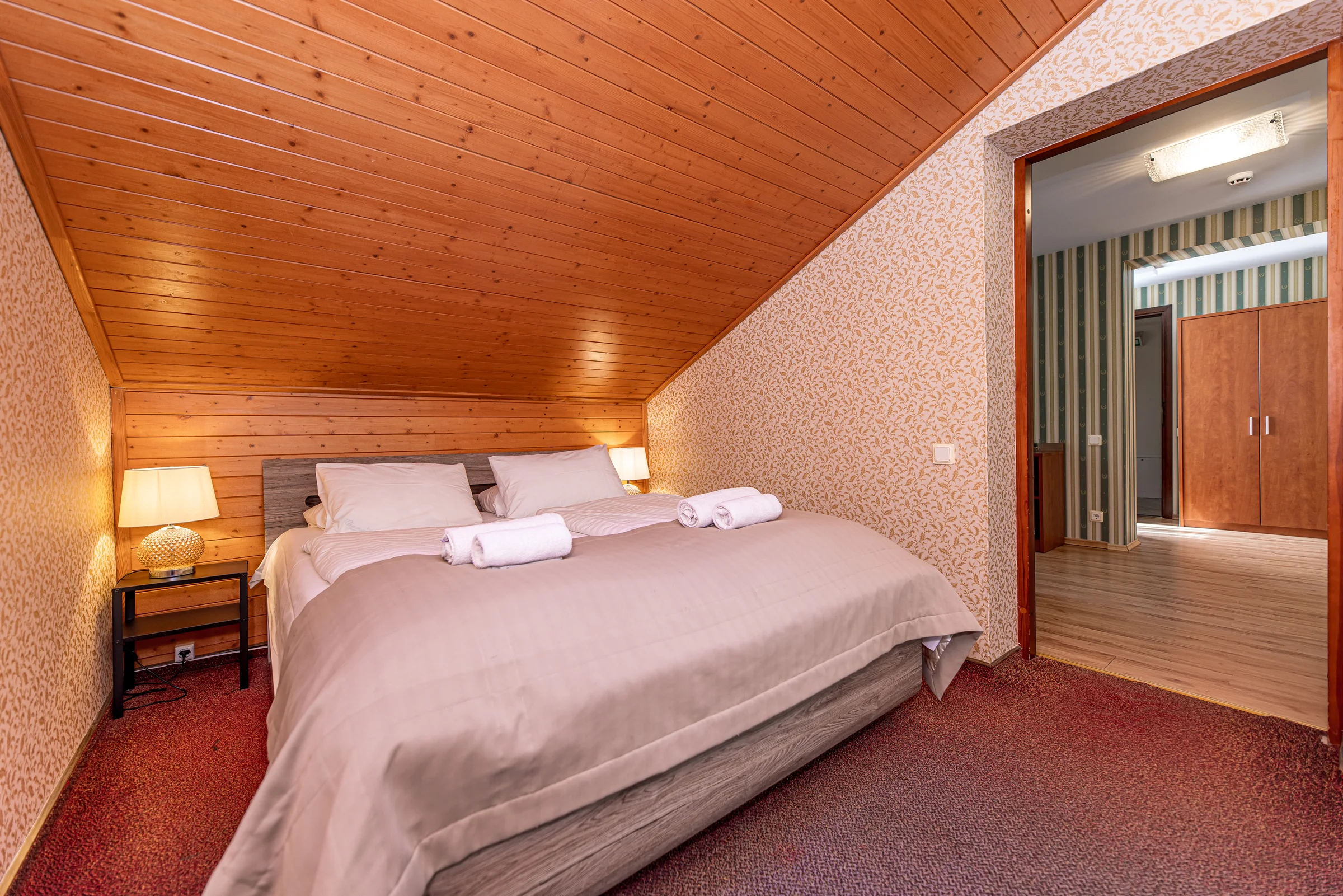 Attic bedroom with a double bed and carpet, the living room seen through the open door