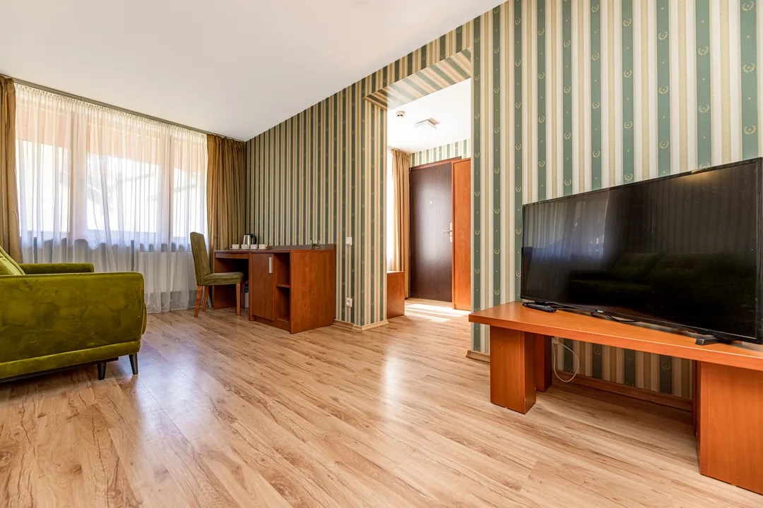 Living room: large TV on a wooden unit, desk with a chair by the window, green sofa