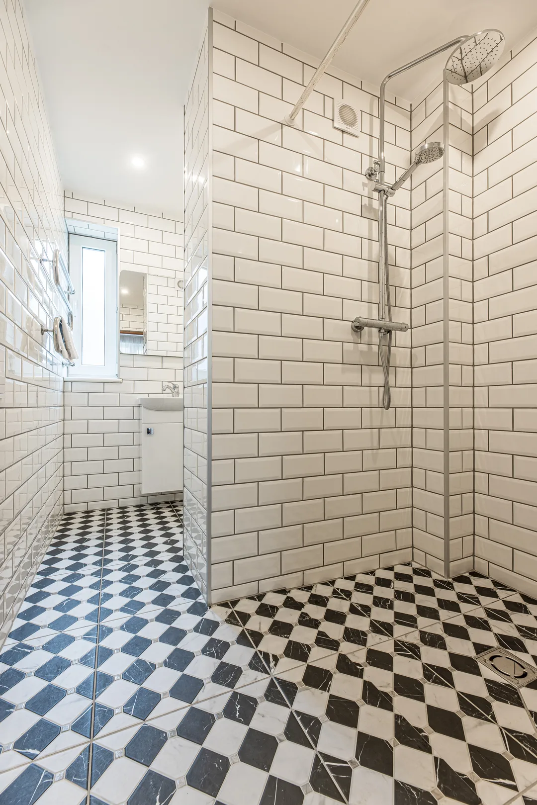 Shower with white wall tiles and a black-and-white tiled floor