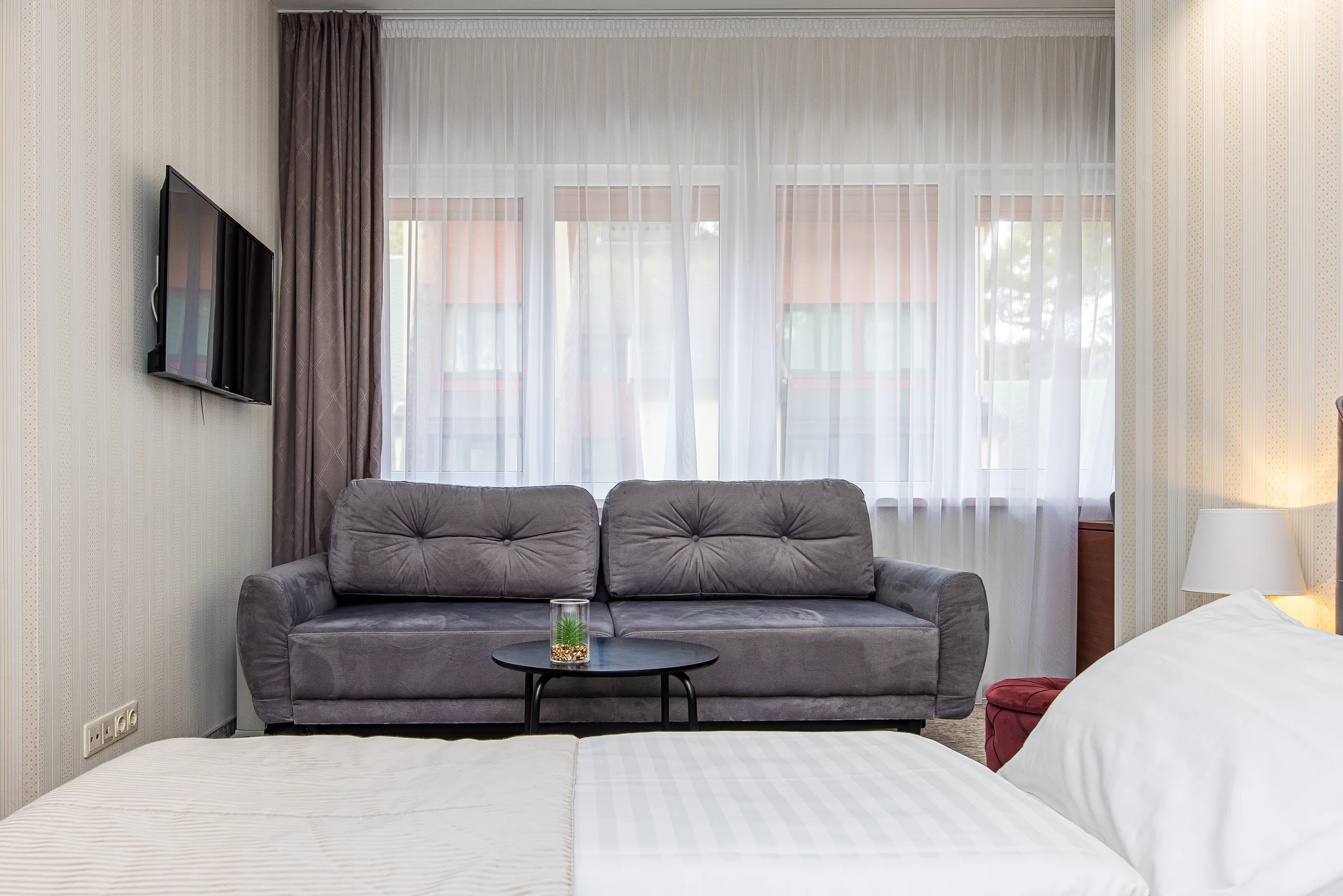Wall-mounted TV, grey sofa under the window and the foot of the bed