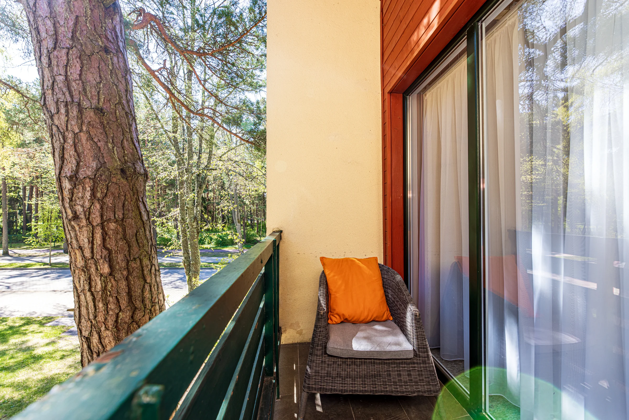 Balcony with a wicker chair, dark railing and a pine trunk