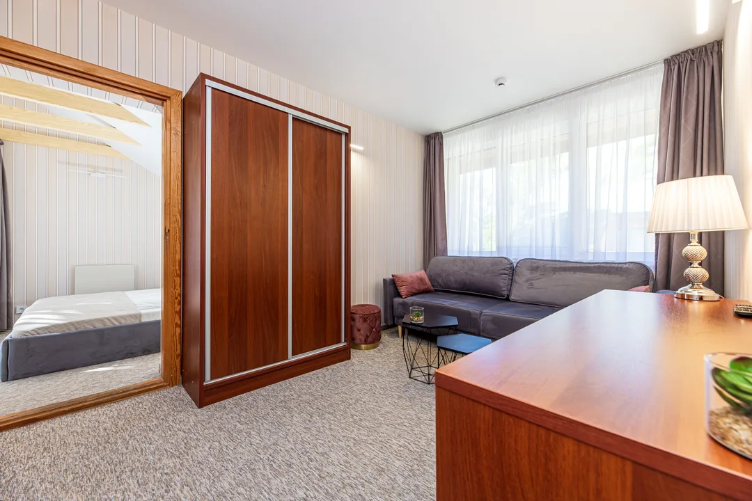 Room with a mirrored wardrobe, sofa and desk with a lamp by the window