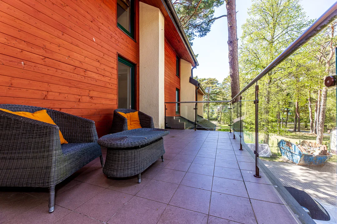Balcony with two wicker armchairs with orange cushions, a glass balustrade and pine trees