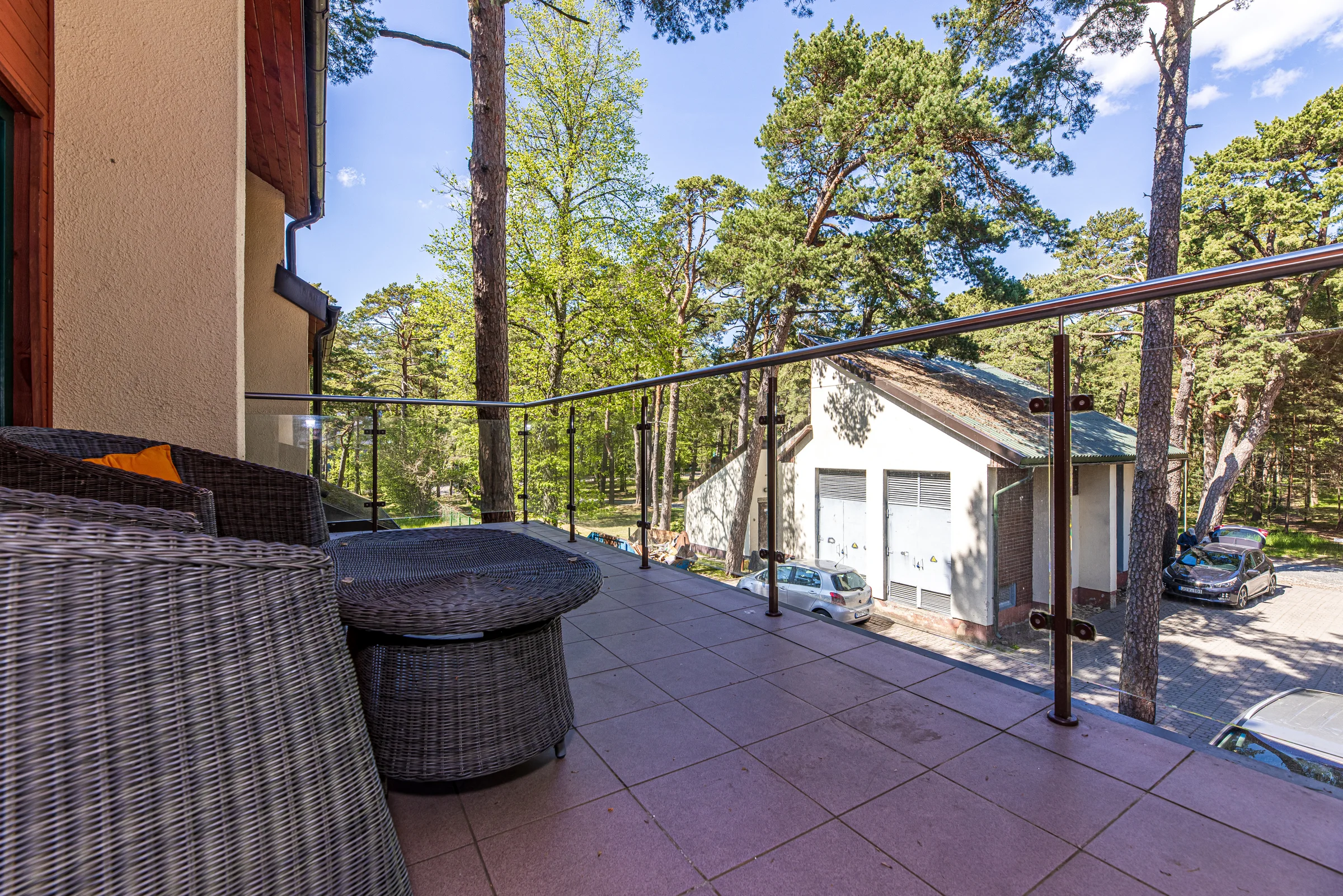 View from the balcony over the glass rail to the pine trees and the courtyard building