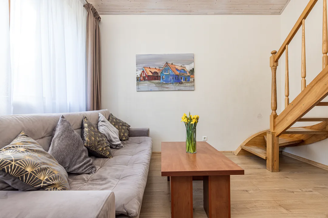 Svetainė su sofa, kavos staliuku ir mediniais laiptais